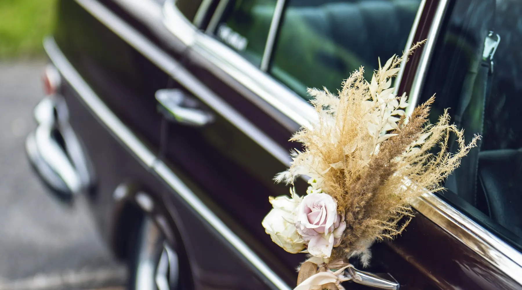 A vintage wedding car door decorated with a dried flower and ribbon bouquet.