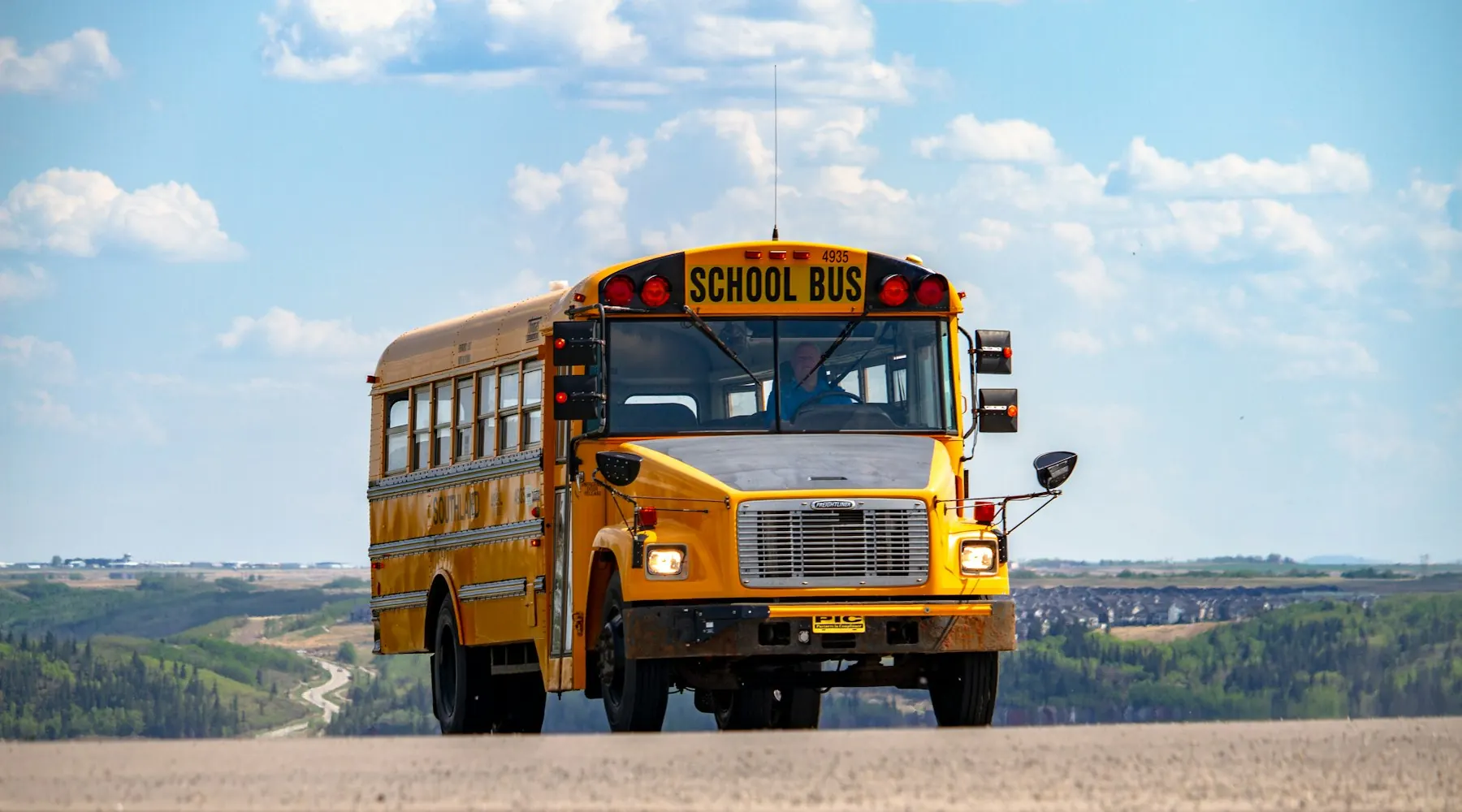 Yellow school bus on a quiet road in bright daylight